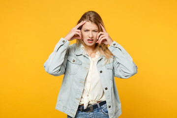 Portrait of jaded exhausted young woman in denim casual clothes looking camera putting hands on head isolated on yellow orange wall background in studio. People lifestyle concept. Mock up copy space.