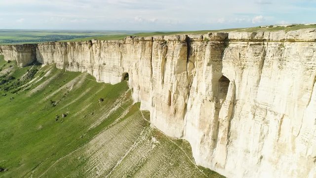 Stunning landscape of White Rock in Crimea with bright green meadow at the foot. Shot. Aerial for the beautiful mountain with flat top and green field on cloudy sky background.