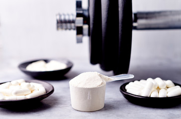 Scoop of Whey Protein, Creatine, Taurine, Beta Alanine capsules and a dumbbell. Bodybuilding food supplements on stone / wooden background. Close up. Copy space.