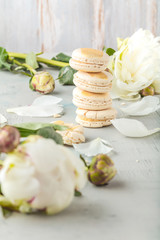 macarons and white peony flowers on wooden surface   