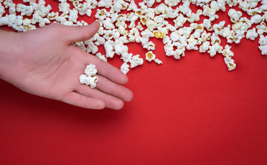 white popcorn on a red background.  hand holding Pop corn