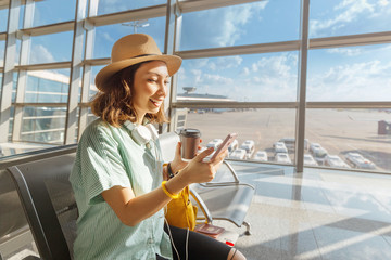Asian girl waiting for departure at the airport on your vacation. Uses a smartphone and drinks...