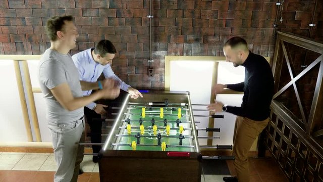 Sport, game concept. Foosball. Three men playing a table football or kicker with miniature players. 4K