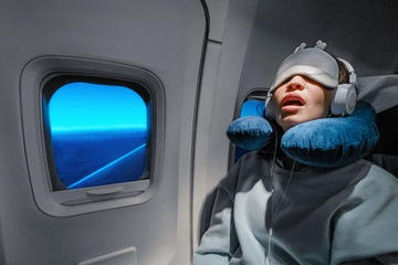 Asian girl sleeping in her seat on the plane near the window in a mask and with a pillow to sleep....
