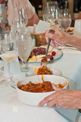 Top, front view, medium distance of a patron's hand holding a fork of spaghetti with red meat sauce , served as a pairing for white, italian wine at a tropical wine tasting event