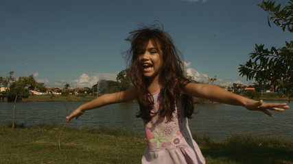  little girl playing happily in the park with pond and blue sky