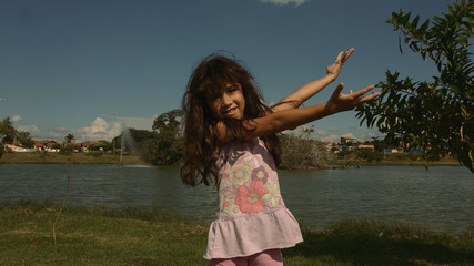  little girl playing happily in the park with pond and blue sky