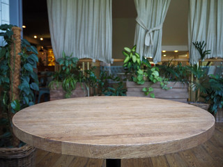 Empty round wooden table in a restaurant on the background of green plants in pots