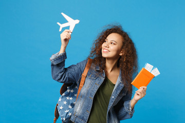 Young african american girl teen student in denim clothes, backpack hold pass isolated on blue wall...
