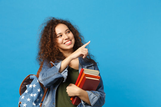 Young african american girl teen student in denim clothes, backpack hold books isolated on blue wall background studio portrait. Education in high school university college concept. Mock up copy space