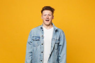 Portrait of surprised young man in denim casual clothes looking camera, keeping mouth open isolated on yellow orange wall background. People sincere emotions, lifestyle concept. Mock up copy space.