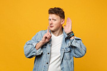 Young man in denim clothes saying hush be quiet with finger on lips shhh gesture, try to hear you...