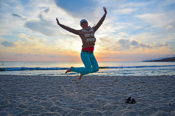 Young girl jumps on the sand by the sea at sunrise.