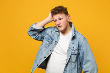 Fototapeta premium Portrait of preoccupied young man in denim casual clothes looking aside, putting hand on head isolated on yellow orange wall background. People sincere emotions lifestyle concept. Mock up copy space.