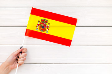 Flag of Spain in hand on white wooden background top view