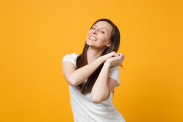 Portrait of smiling joyful young woman in white casual clothes clenching fists, looking camera isolated on bright yellow orange wall background in studio. People lifestyle concept. Mock up copy space.