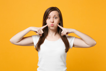 Portrait of funny young woman in white casual clothes pointing index fingers on blowing cheeks isolated on bright yellow orange wall background in studio. People lifestyle concept. Mock up copy space.