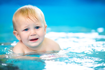 Fototapeta na wymiar Cute sad baby boy learning to swim in special pool for little children