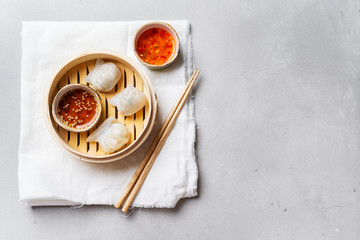 Traditional chinese steamed dumplings Dim Sums HAR GOW in bamboo steamer with sauces and chopsticks atop cotton textile on light surface with copy space. Flat lay Asian food background.