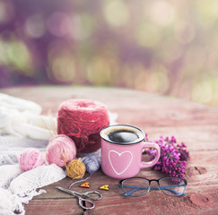  Women's hobby. Crochet and knitting. Working space. Bouquet of lilac in a cup, balls of yarn, needles, scissors, knitwear, crochet hooks on the wood table  in the cozy home. 