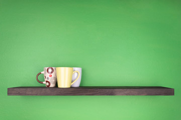 a dark color shelf with texturing wood is installed on a green wall; on the shelf there are three cups in a group with leavs