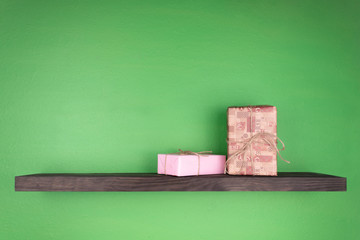 two gift boxes on a dark color shelf with wood texture mounted on a green wall