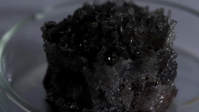 Beautiful unusual gray-black crystal stone cassiterite with a metallic sheen standing in the glass stand. Stock footage. Close up for shining crystal standing on the table.