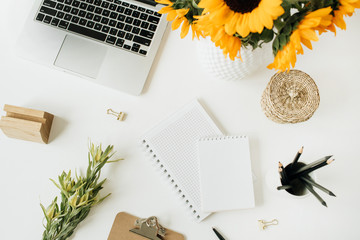 Flatlay of home office desk workspace with laptop, notebook, yellow sunflowers bouquet on white...