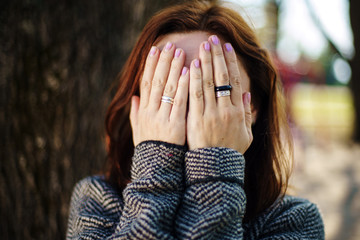 Woman covers her face with her hands. Rings on fingers.