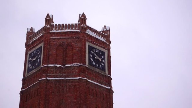 Big old brick tower with clock in snowfall in winter, isolated slow motion