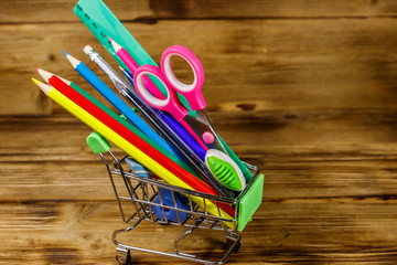 Buying school supplies. Shopping cart with school supplies on a wooden background. Back to school concept