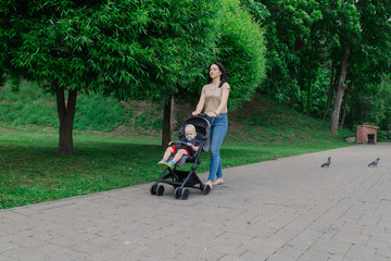 Beautiful woman with a child in a pram walks through a summer park.