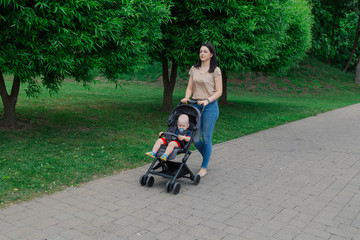 Fototapeta na wymiar Beautiful woman with a child in a pram walks through a summer park.