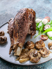 Close-up roasted lamb with mushrooms, spices and herbs on a round plate on a concrete background....