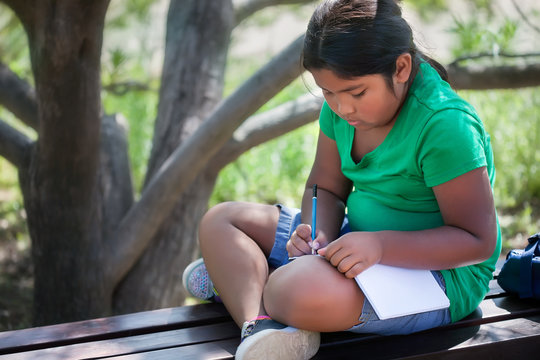 A homeschooled child sitting in an outdoor garden in a relaxed pose, while solving or learning elementary school level subjects.