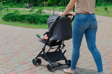 Obraz premium Beautiful woman with a child in a pram walks through a summer park.