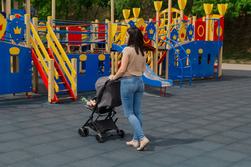 Young mom with a baby in a stroller at the playground.