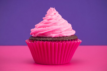 A Single Pink Frosted Chocolate Cupcake on a Pink and Purple Surface