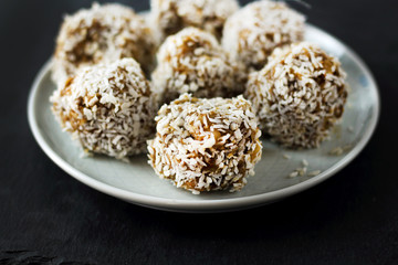 vegetarian raw healthy diet  no bake candies dessert sweets without sugar and gluten-free with coconut, proper nutrition snack on blue plate and black slate background, free copy space for text