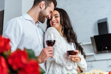 selective focus of happy couple holding glasses with red wine and looking at each other