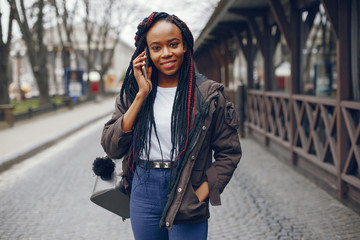 Fototapeta premium A beautiful and stylish dark-skinned girl with long hair walking in the autumn city with backpack and mobile phone