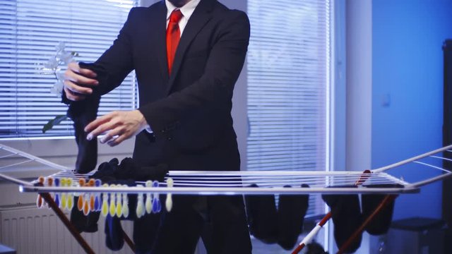 Businessman hand washed clothes doing housework 4K. Medium shot of headless male businessman in focus while picking hanged black socks. Windows in background