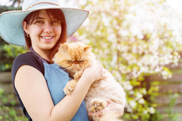Photo of smiling woman in hat holding ginger cat in garden