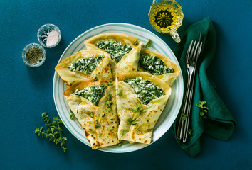 Traditional Italian pancakes crepes with spinach and ricotta on a served blue table. healthy vegetarian diet