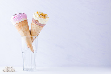 Ice cream with chocolate and nuts on a white background. Two ice cream cones in a glass. Summer milk dessert in a waffle cone. Copy space