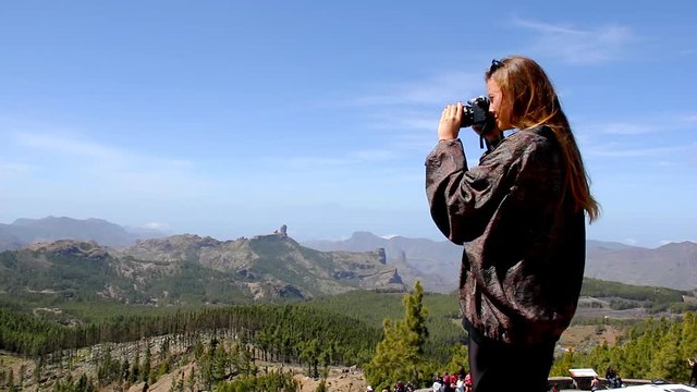 Young woman taking photos with dslr camera on mountain top in Gran Canaria, Spain. Blonde girl tourist capturing beautiful landscape of Roque Nublo from Pico de las Nieves in Canary Islands