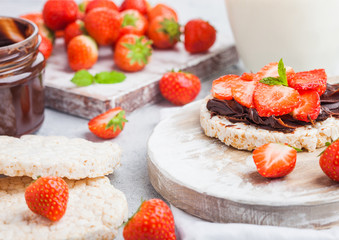 Healthy organic rice cakes with chocolate butter and fresh strawberries on wooden board and glass of milk on light stone kitchen background. Top view.