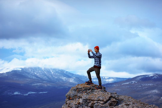 Man taking photo on smartphone on the peak of the mountain