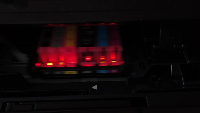 The moving carriage of an inkjet printer showing the cartridges lit by red LED lights.