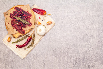 Basturma, dried tenderloin of beef meat, jerky, thinly sliced. Dry rosemary, pepper mix, chili, garlic on vintage linen cloth. Delicious food on a wooden board, stone background, copy space, top view.